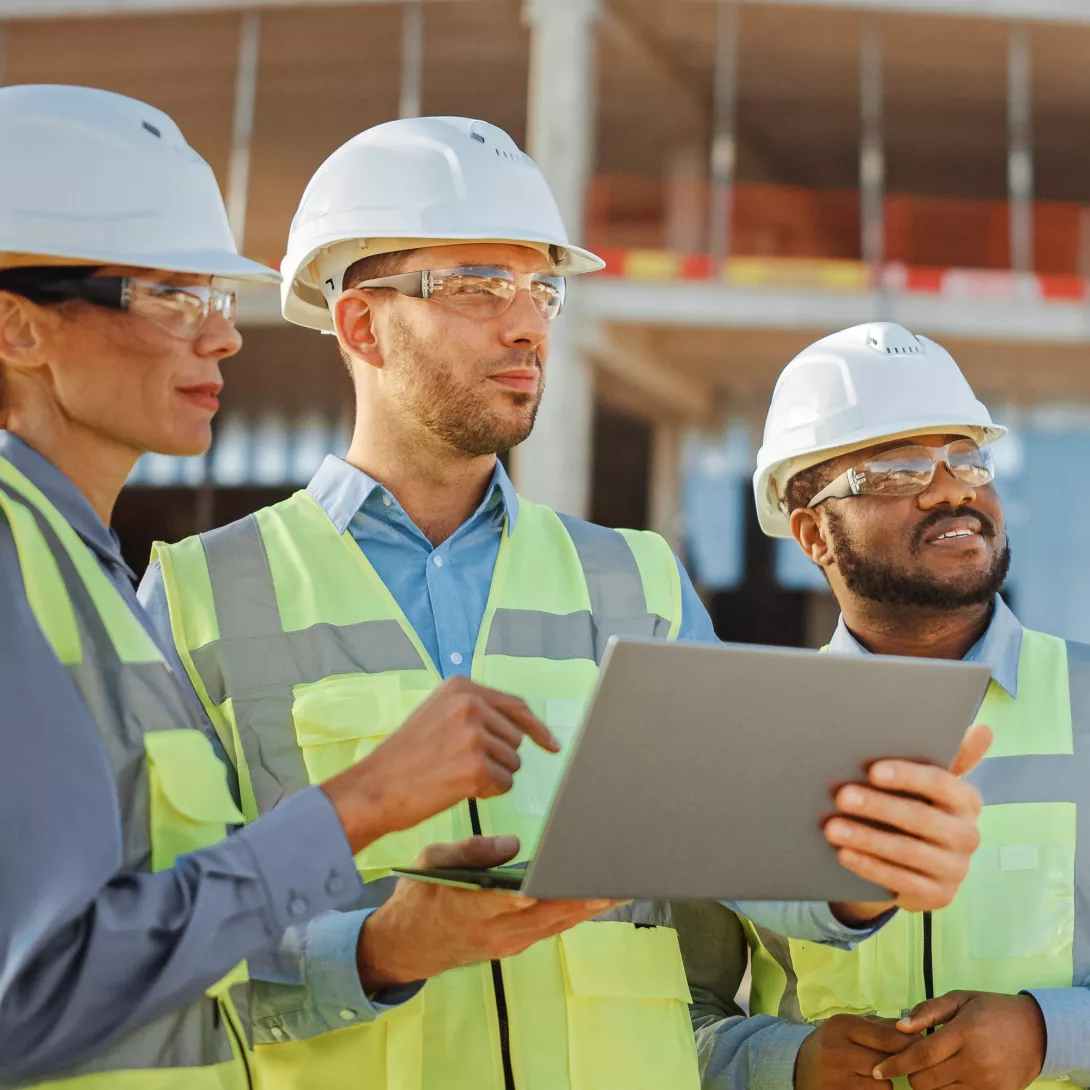 Zwei Männer und eine Frau sind auf einer Baustelle und einer der Männer hält einen Laptop