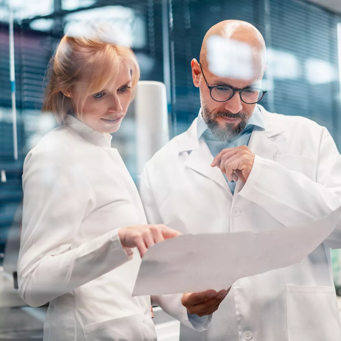 A woman and a man in white lab coats check a paper