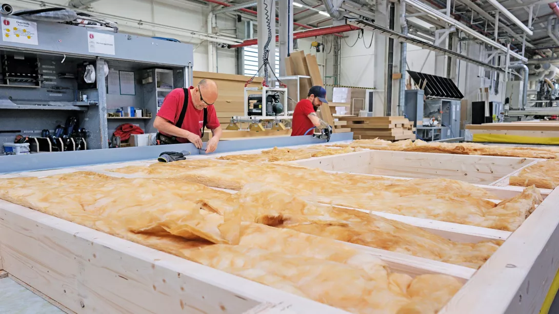 In der weiteren Produktion werden die Riegelwerke der Wände von den Mitarbeitenden mit Leerrohren für die spätere Elektroinstallation bestückt. Zusätzlich werden die Holzständer mit mineralischer Dämmwolle ausgestattet – sie wird auf nachhaltige Weise aus recyceltem Altglas gewonnen.