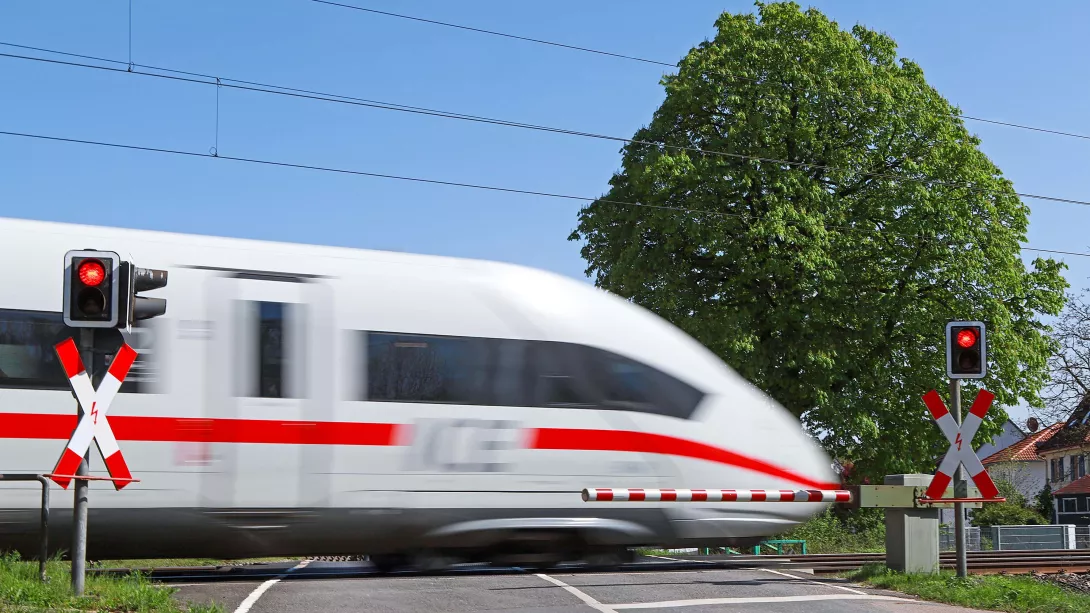 Der Hochgeschwindigkeitszug ICE passiert einen beschrankten Bahnübergang